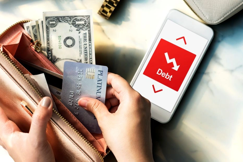 woman pulling a credit card from her wallet next to a phone showing a debt alert